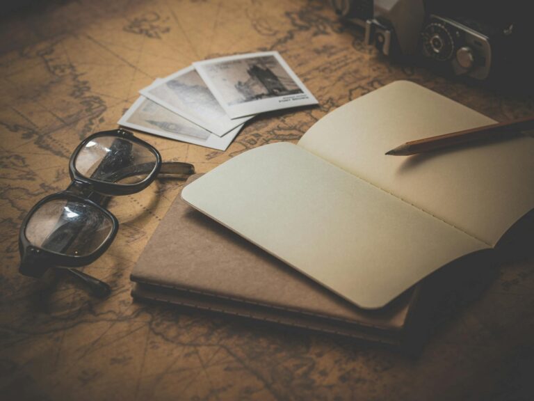 Stylized flat lay of a vintage travel journal with eyeglasses, photos, and a map background.