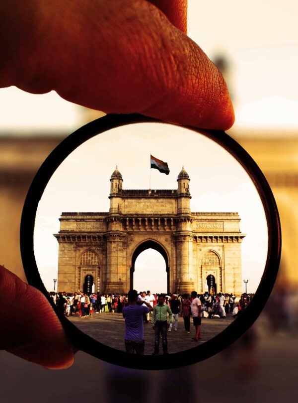 Artistic view of the Gateway of India through a camera lens filter with vibrant colors and bustling crowd.